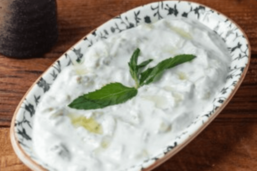A rectangular ceramic dish filled with creamy cucumber yogurt dip, garnished with a fresh mint sprig and a drizzle of olive oil, placed on a wooden table.