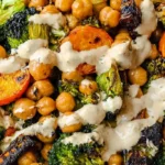 Roasted vegetables with chickpeas, broccoli, Brussels sprouts, and sweet potatoes drizzled with creamy dressing in a white bowl.
