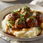 Juicy meatballs in rich brown gravy served over creamy mashed potatoes with parsley garnish in a bright kitchen.
