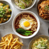 Food collage showing ten different noodle, pasta, soup, and potato dishes, including stir-fries, creamy pastas, spicy noodle soup, fries with dipping sauce, and rice noodles with tofu, all arranged in a bright, clean layout.