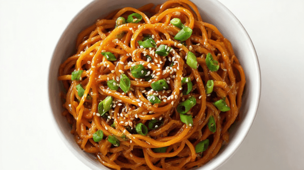 Bowl of saucy noodles topped with sliced green onions and sesame seeds.