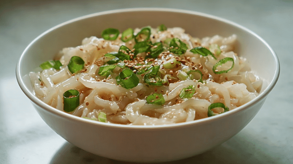 Wide bowl of hand-pulled noodles topped with sliced green onions and toasted sesame seeds.