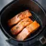 Air fryer cooking frozen salmon on a plate with herbs