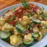 Creamy corn and cucumber salad served in a bowl, garnished with herbs.