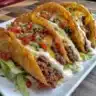 Crispy ground beef tacos filled with toppings on a plate
