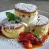 Fluffy Japanese soufflé pancakes stacked high on a plate, topped with syrup and berries.