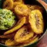 Plate of golden-brown fried plantains garnished with fresh herbs