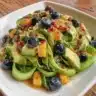 Mango cucumber salad topped with blueberries and avocado in a colorful bowl.
