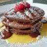 Delicious chocolate pancakes stacked with syrup and berries on top