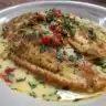 Italian seasoned tilapia dish garnished with herbs and lemon