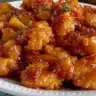 Plate of baked orange chicken garnished with green onions and served with rice.
