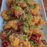 Crispy sesame chicken served with garnishes on a plate