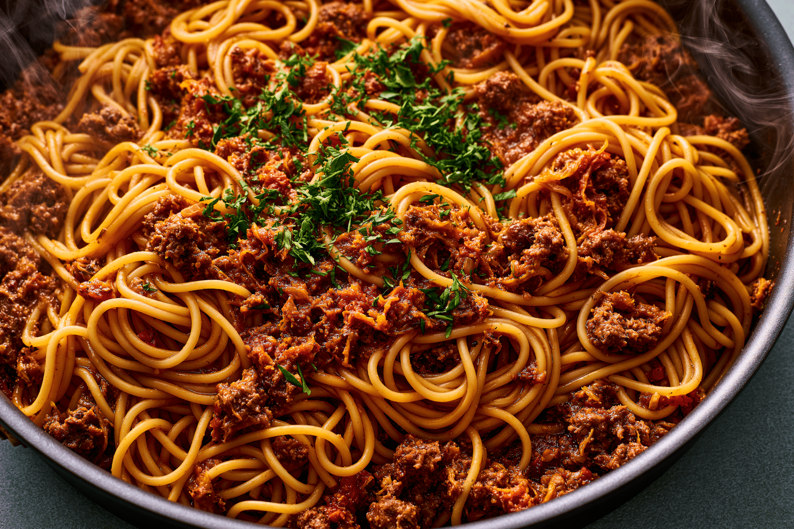 A close-up overhead shot of a perfectly cooked dirty spaghetti in a large, deep pan, garnished with fresh herbs, steam rising slightly, indicating it just finished cooking. Focus on the rich texture and vibrant colors of the dish.
