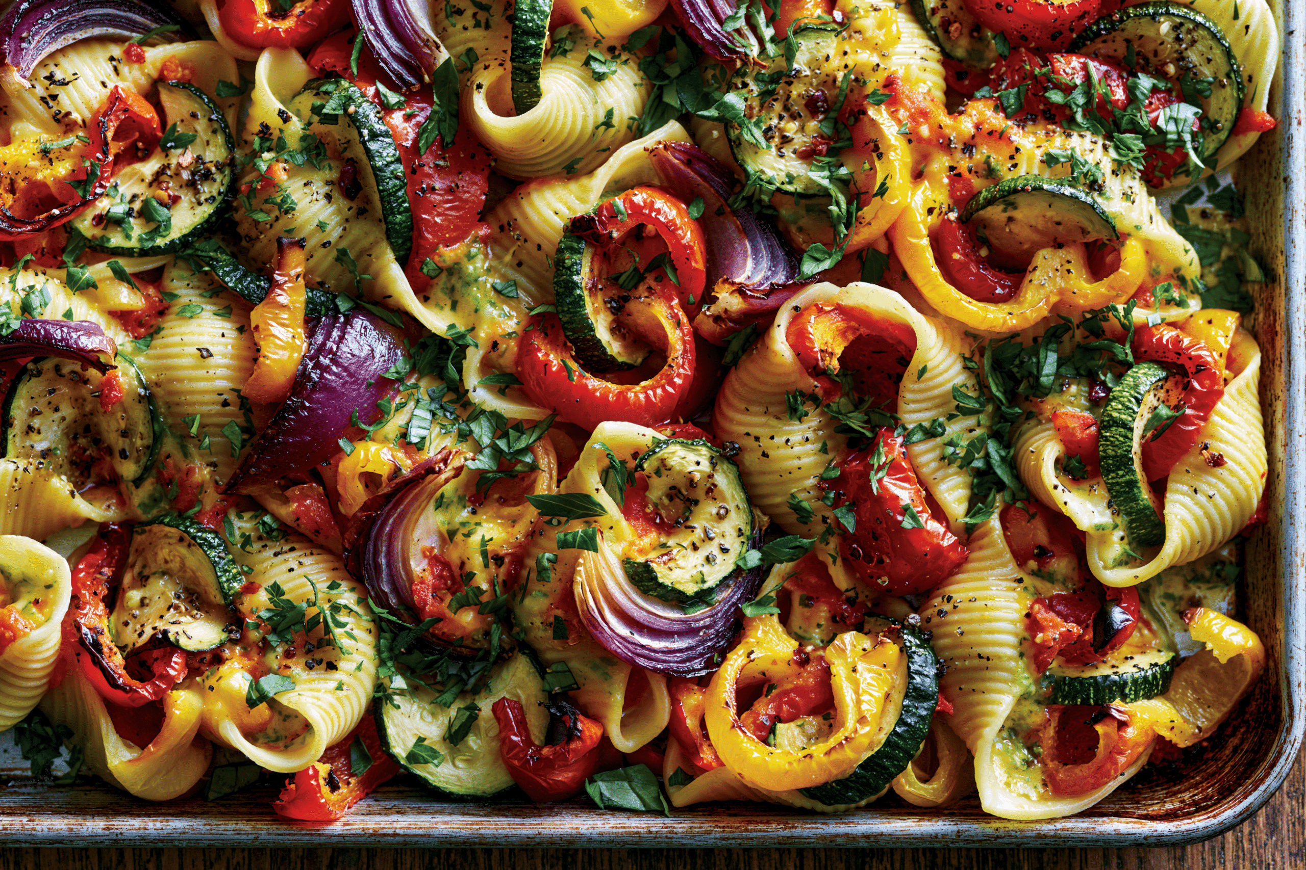 A colorful vegetarian baked filled pasta dish with roasted bell peppers, zucchini, and red onion, topped with fresh herbs, on a baking tray.