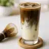 Chilled iced hojicha latte with creamy oat milk and roasted green tea powder on top.