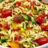 Colorful summer orzo pasta salad with vegetables and herbs in a bowl